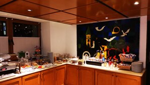 A kitchen with wooden cabinets, a countertop with various food items, and a large window with a view of a cityscape. - Apart Business Hotel  (Stuttgart)