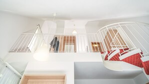 A spacious interior with a high ceiling, a staircase with white railings, and a view of a room with a wooden door. - Apart Business Hotel  (Stuttgart)