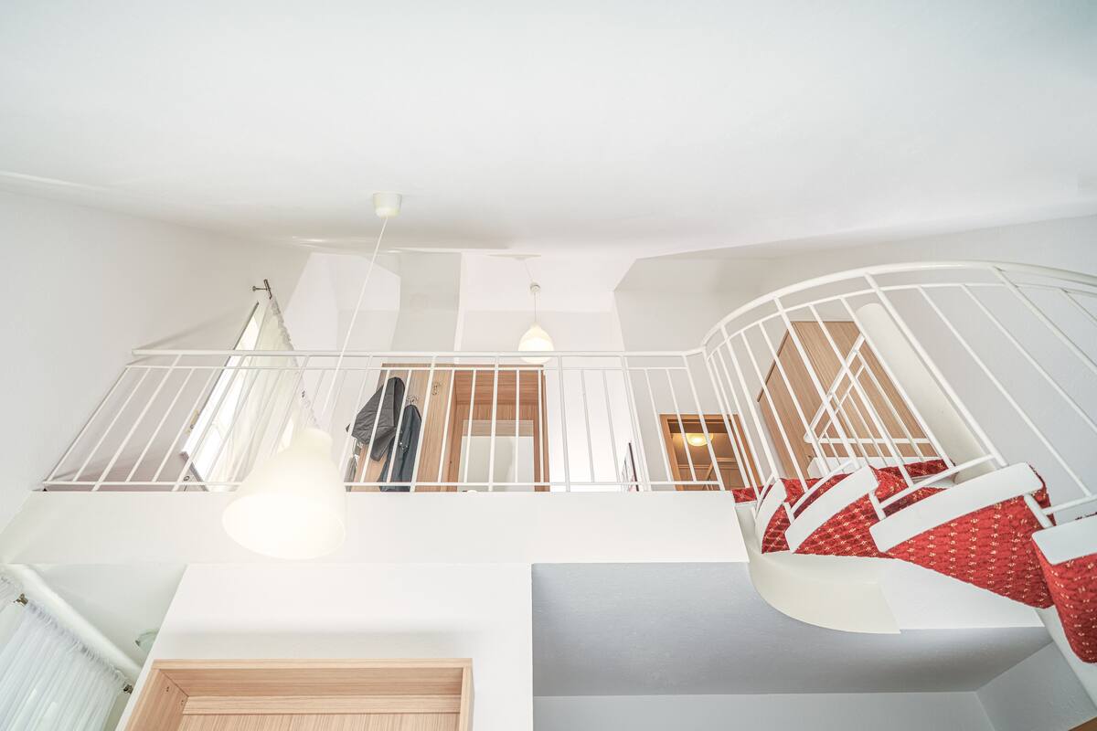 A spacious interior with a high ceiling, a staircase with white railings, and a view of a room with a wooden door.