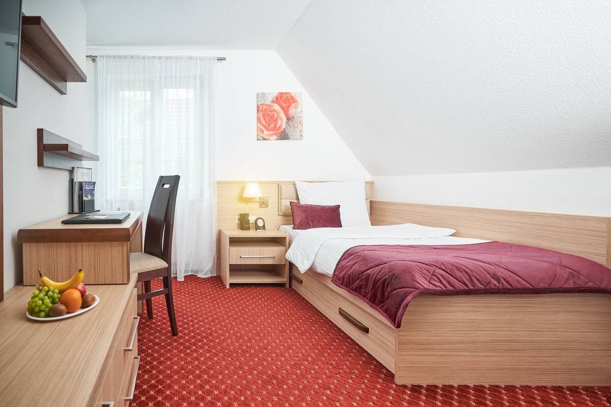 A hotel room with a bed, desk, chair, and a fruit bowl.
