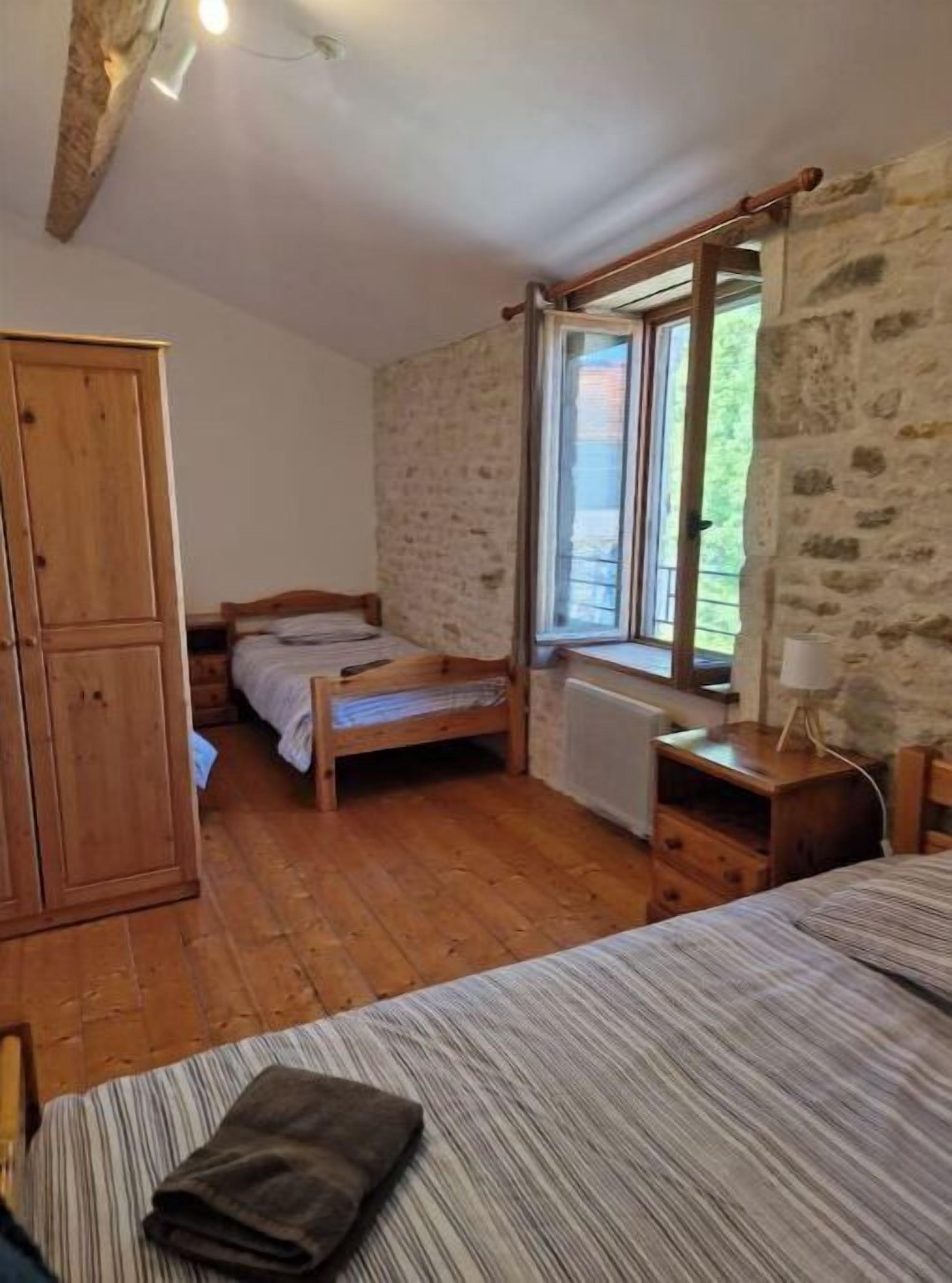 A bedroom with a wooden wardrobe, a single bed, a smaller bed, a window with curtains, and a radiator.