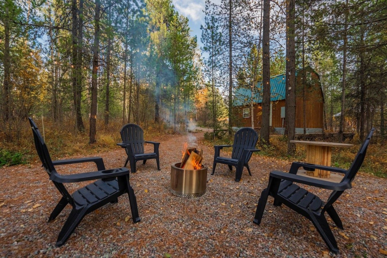 A forest setting with a fire pit and chairs arranged for outdoor seating.