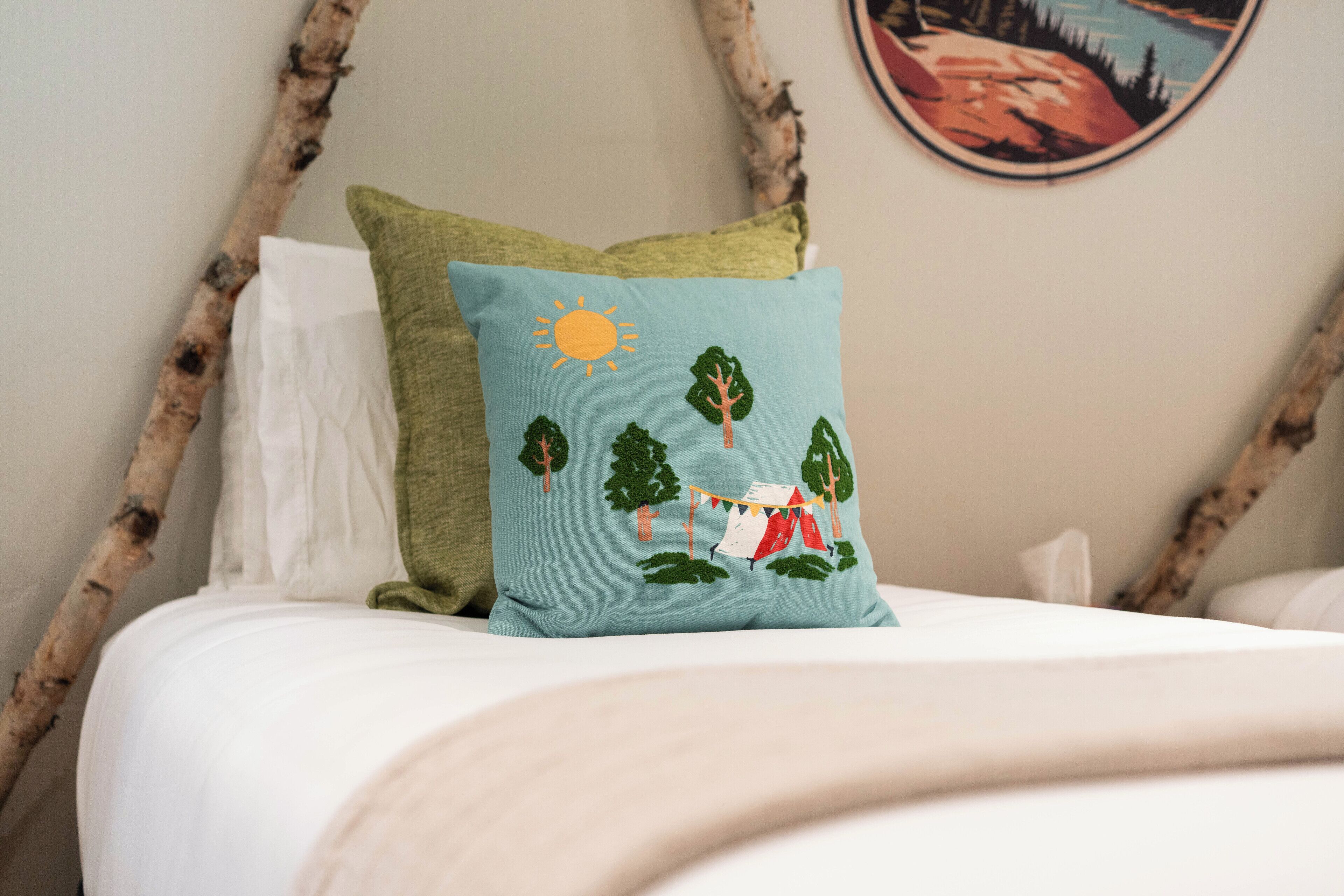 A bed with a white sheet, a green pillow with a camping scene, and a white pillow.