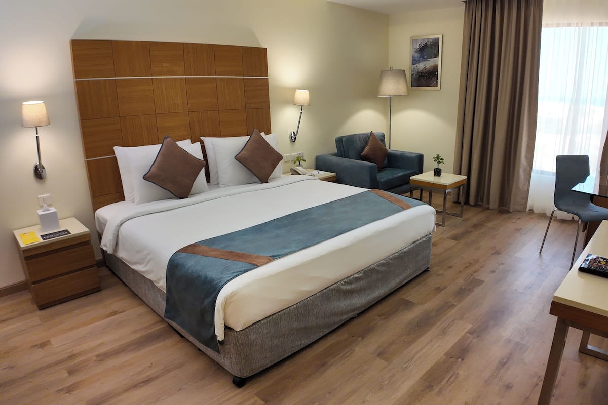 A hotel room with a large bed, a desk, a chair, a nightstand, and a lamp.