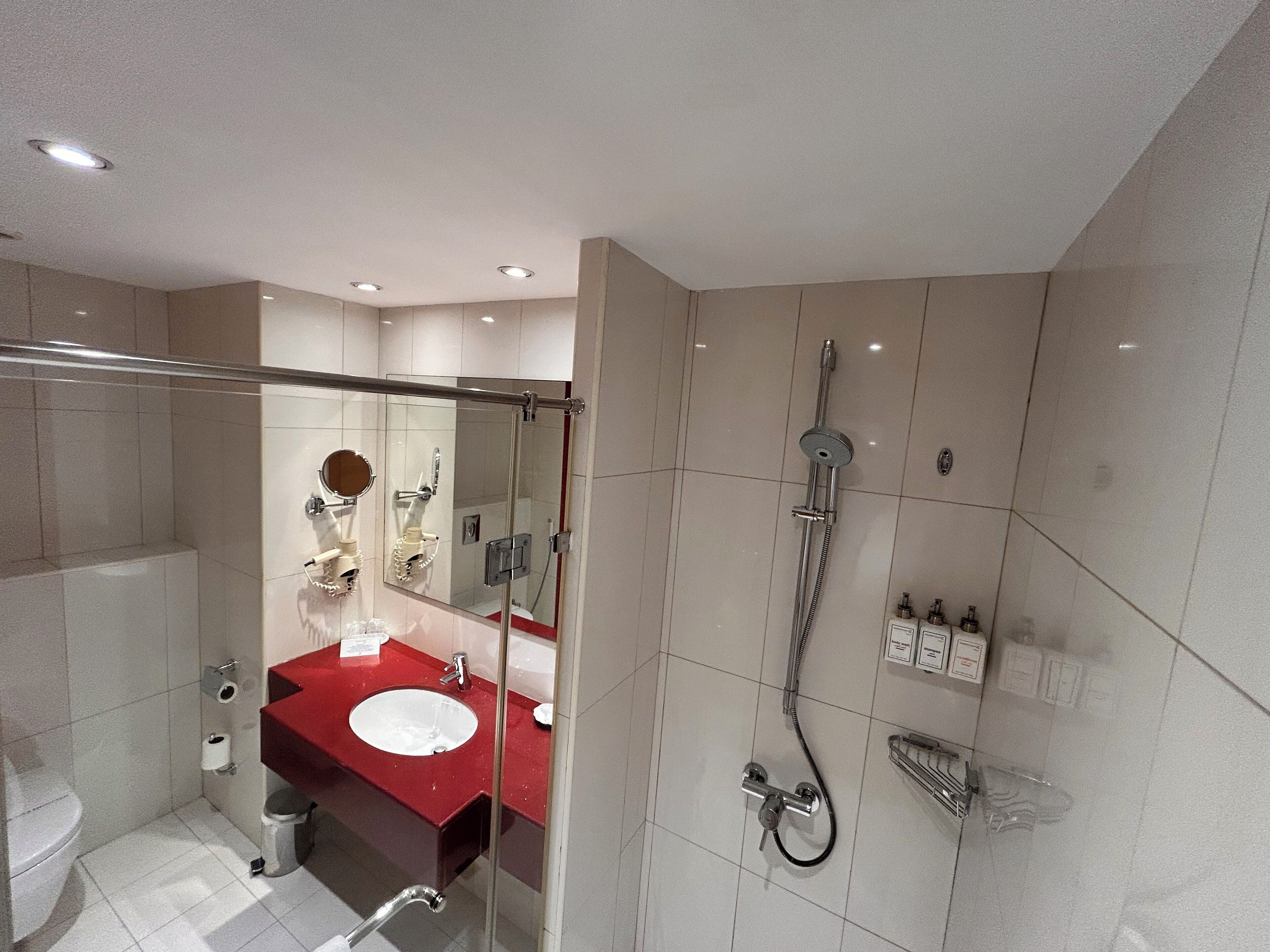 Un baño moderno con ducha de vidrio, lavabo rojo y un espejo grande.