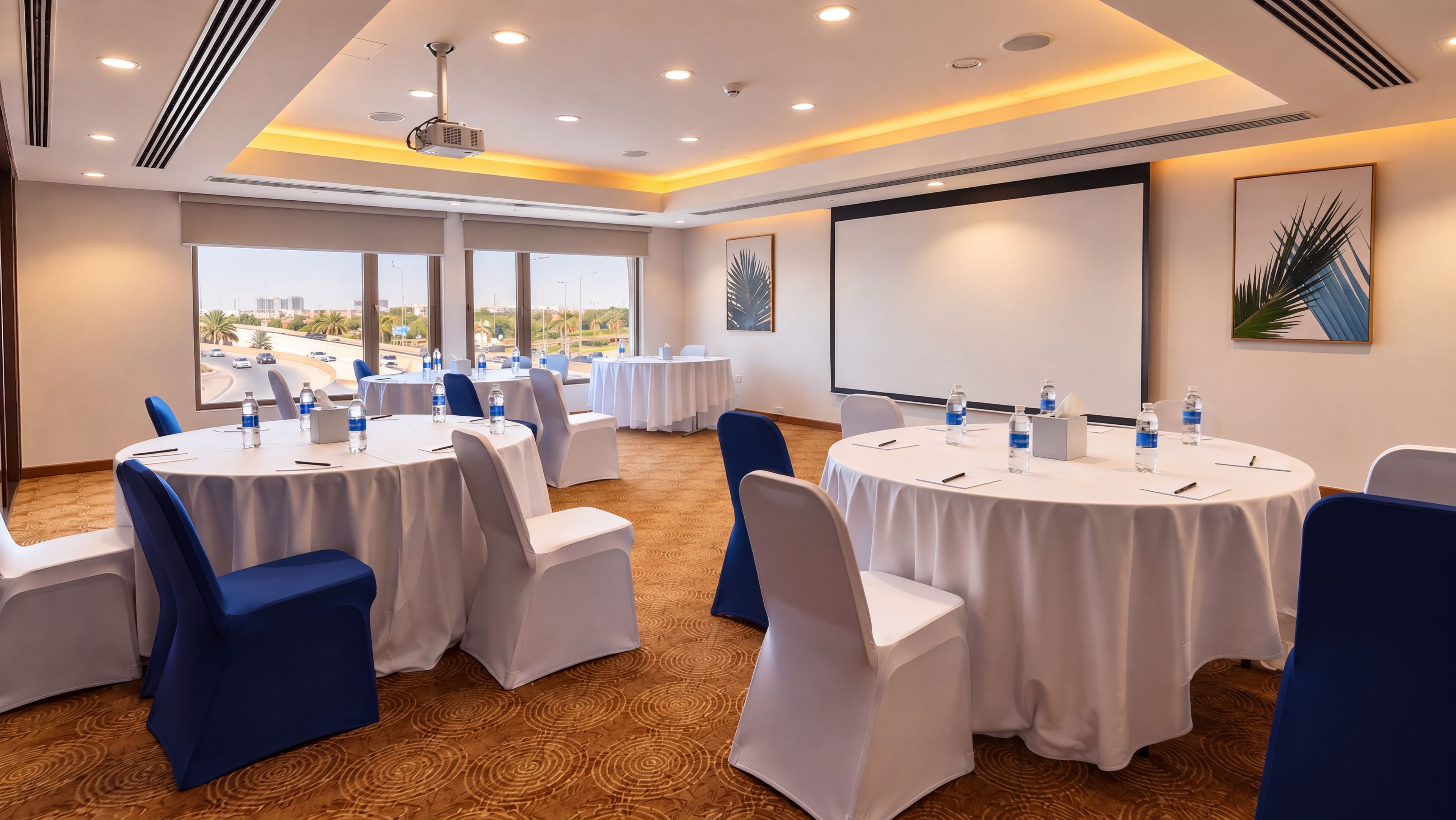 A conference room with round tables, chairs, and a projector screen.