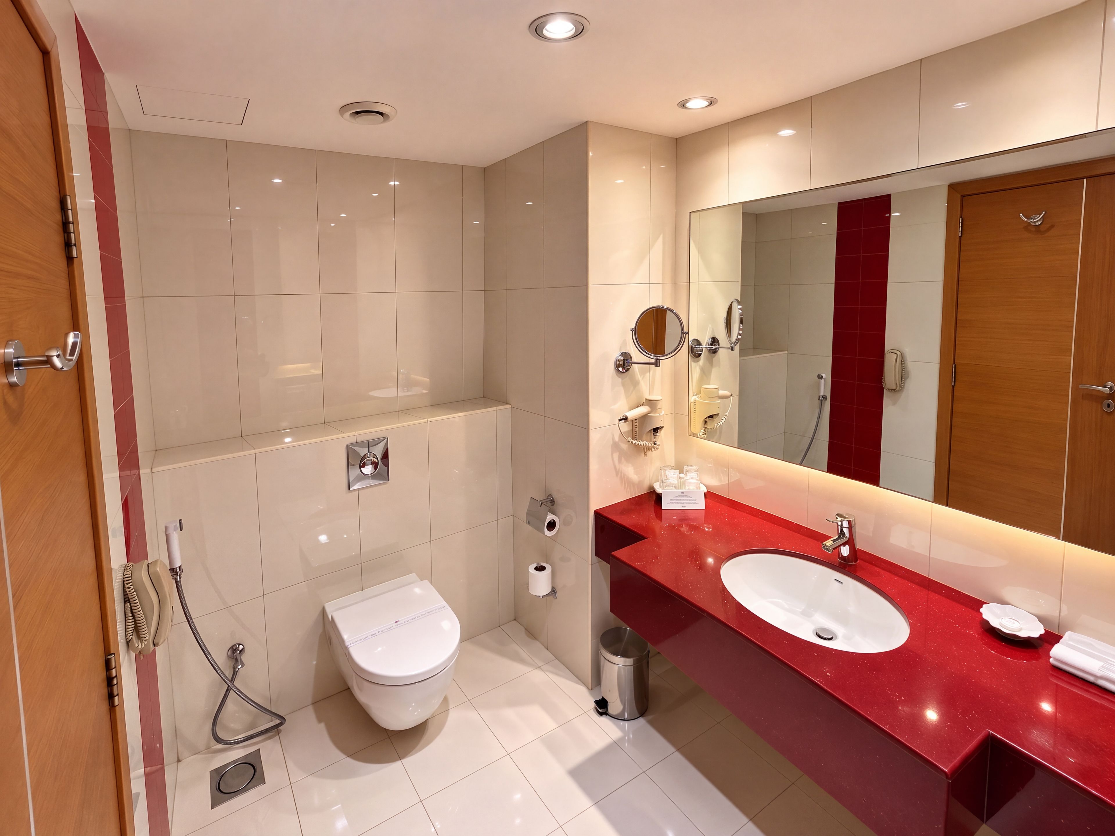 A modern bathroom with a red countertop, two sinks, a toilet, a shower, and a large mirror.