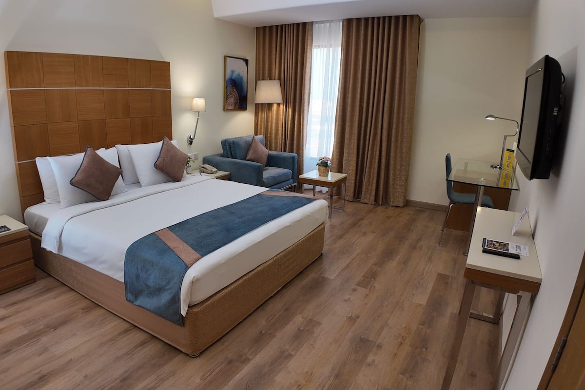 A hotel room with a large bed, a desk, a chair, a TV, and a lamp.