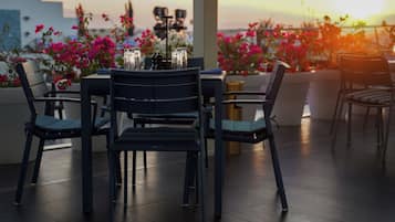 Una terraza con mesa y sillas, rodeada de macetas con plantas y flores.