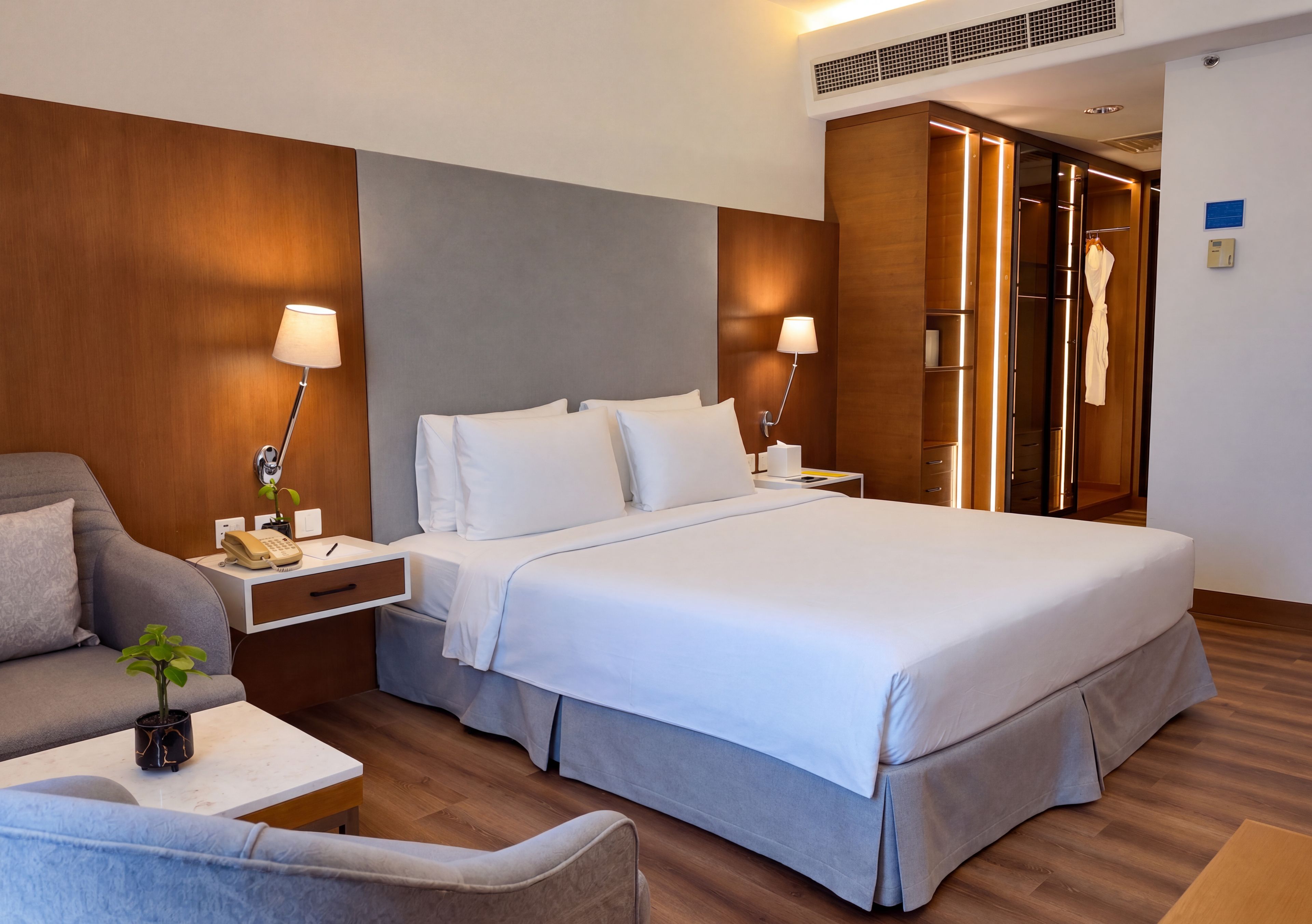 Een hotelkamer met een groot bed, nachtkastjes, een stoel, een bureau, een plant en een kledingkast.