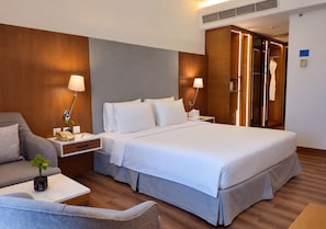 Una habitación de hotel con una cama grande, mesitas de noche, una silla, un escritorio, una planta y un armario.