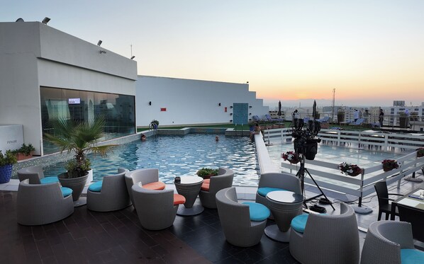 A rooftop pool area with lounge chairs and a view of the city at sunset. - Golden Tulip Muscat (Muscat)