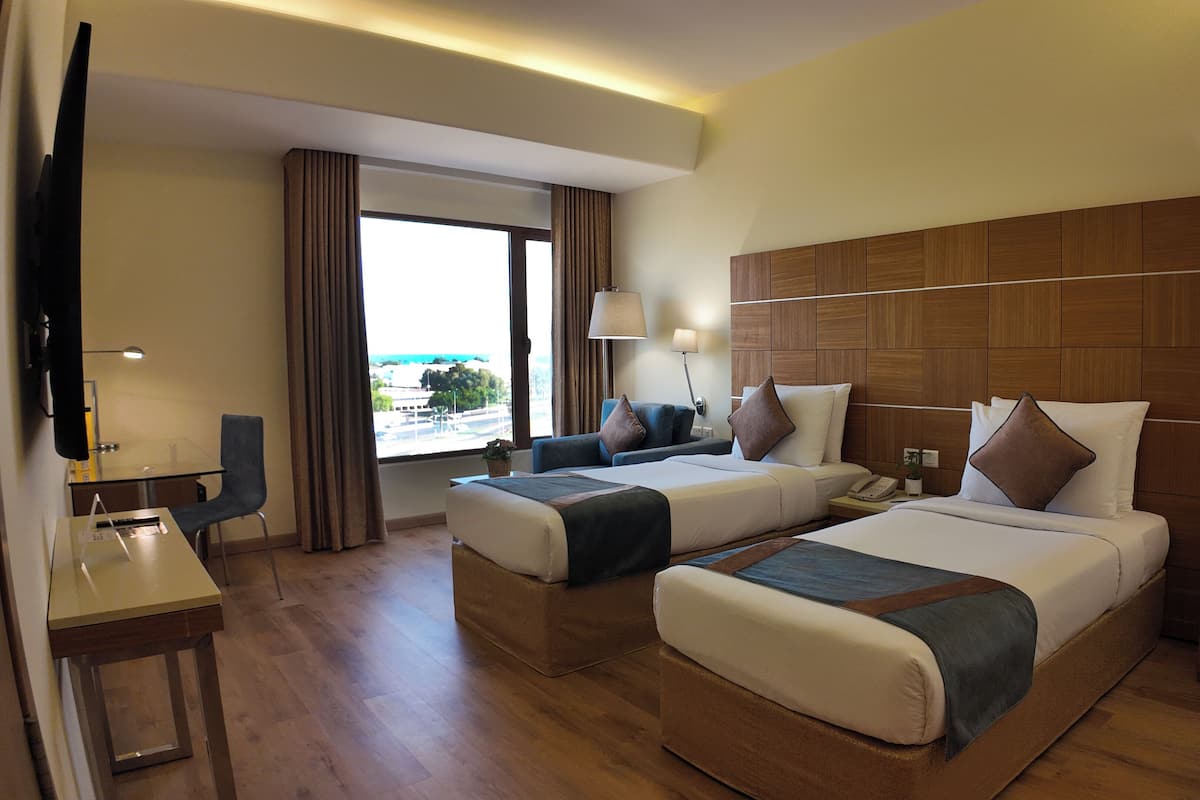 A hotel room with two beds, a desk, a chair, a TV, and a window with curtains.