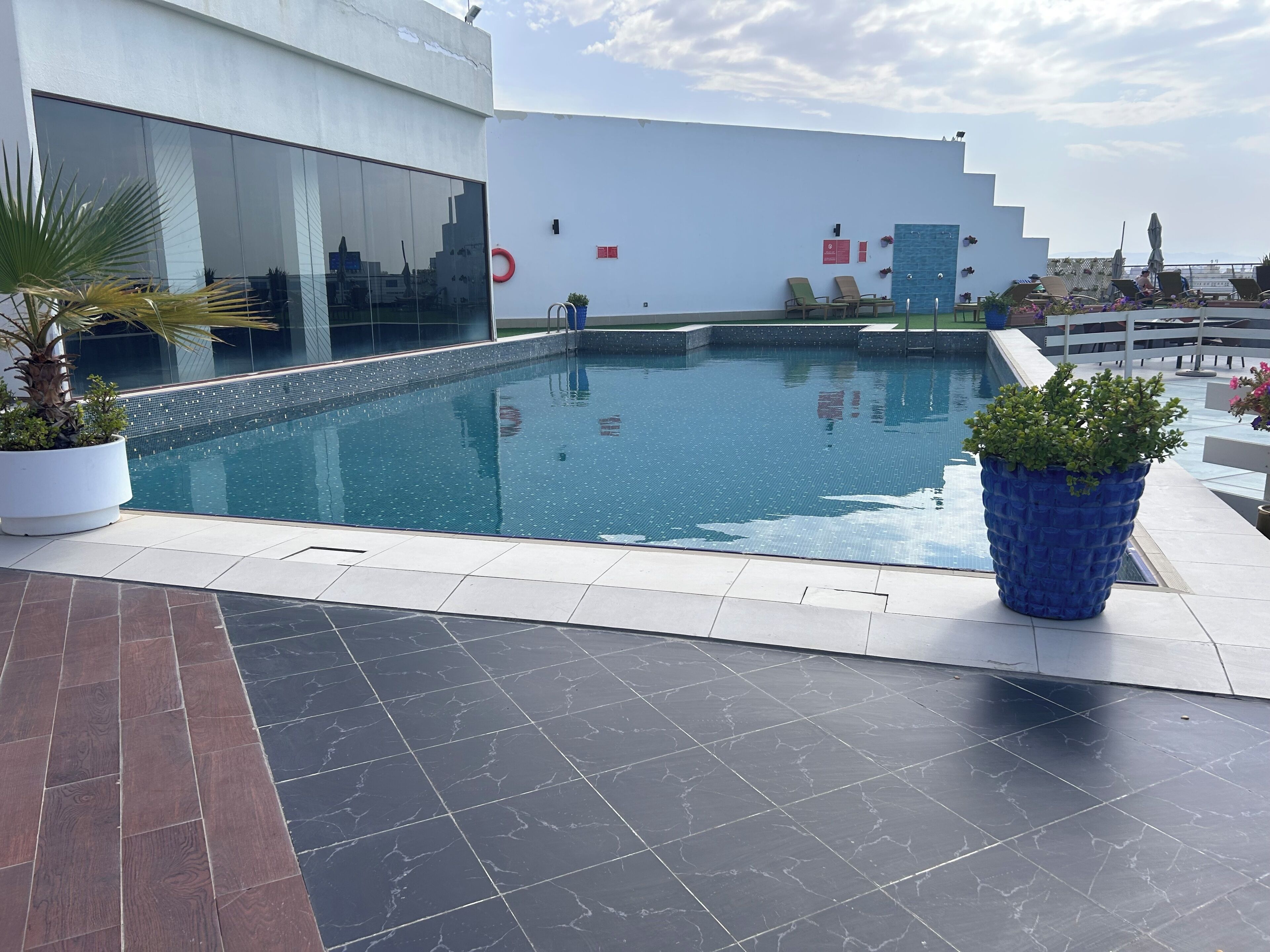 A rooftop pool area with a clear view of the city skyline, a modern building with large windows, and a few lounge chairs.