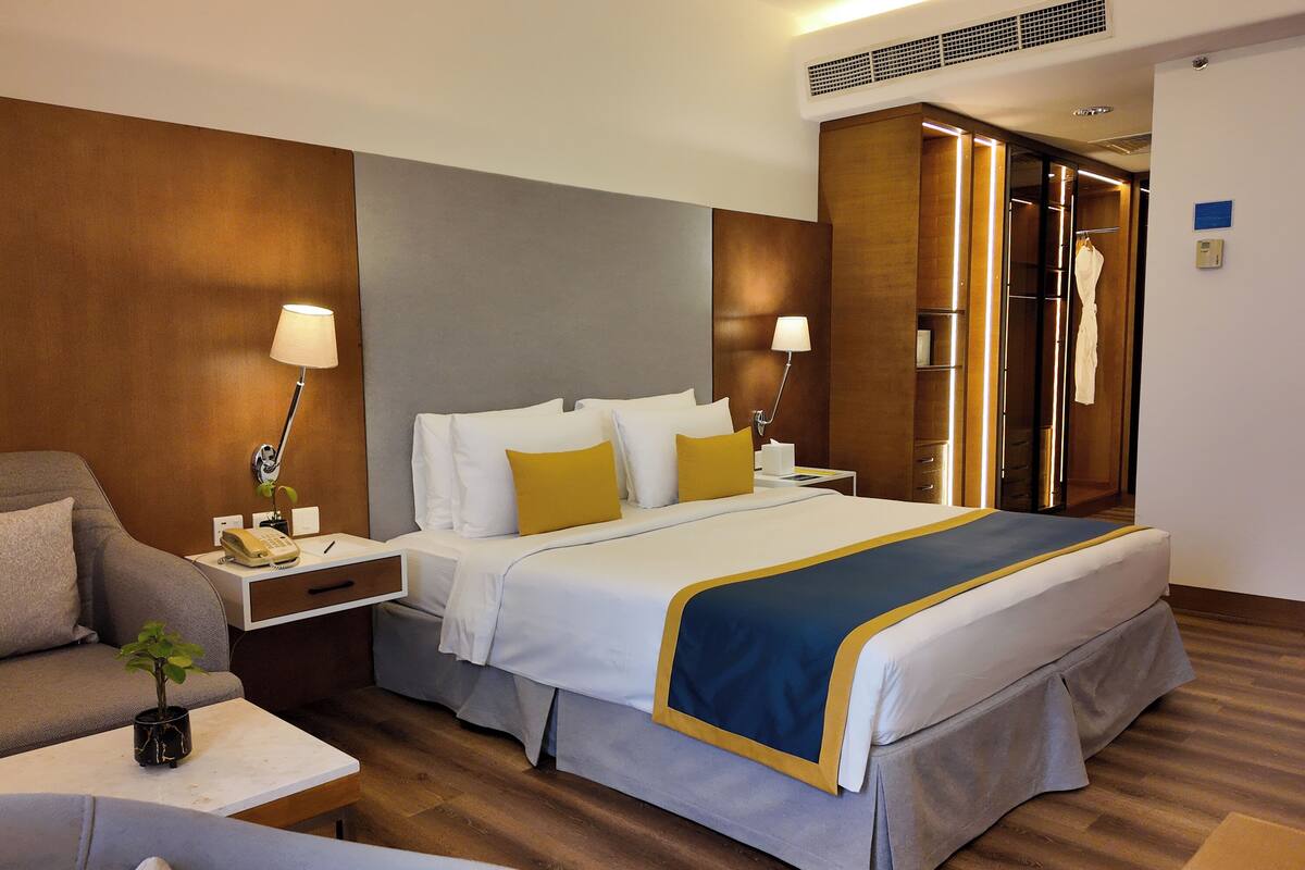 A hotel room with a large bed, bedside tables, a desk, a chair, a wardrobe, and a mirror.