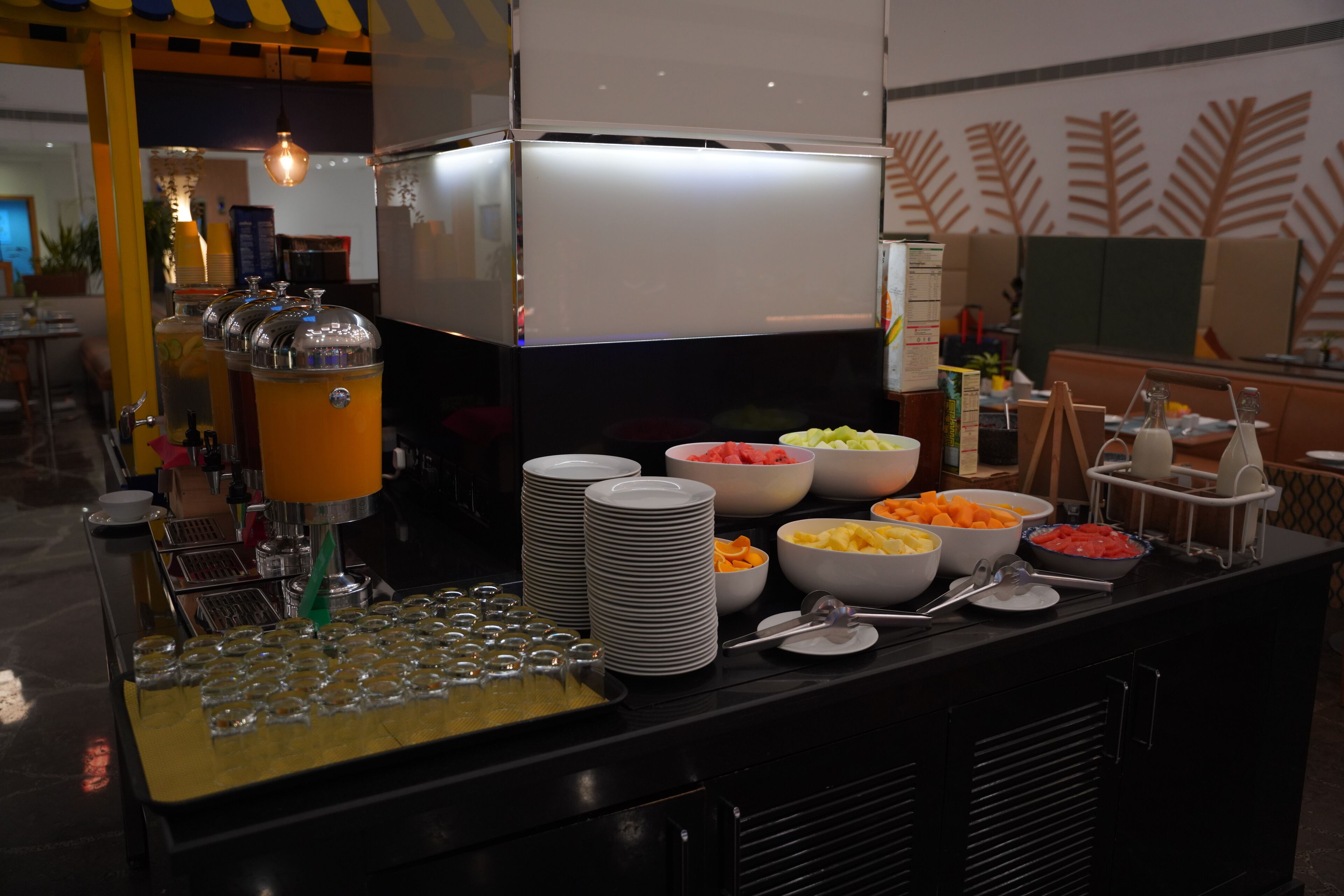 A buffet setup with various food items and beverages, including bowls of fruits and vegetables, and a beverage dispenser.