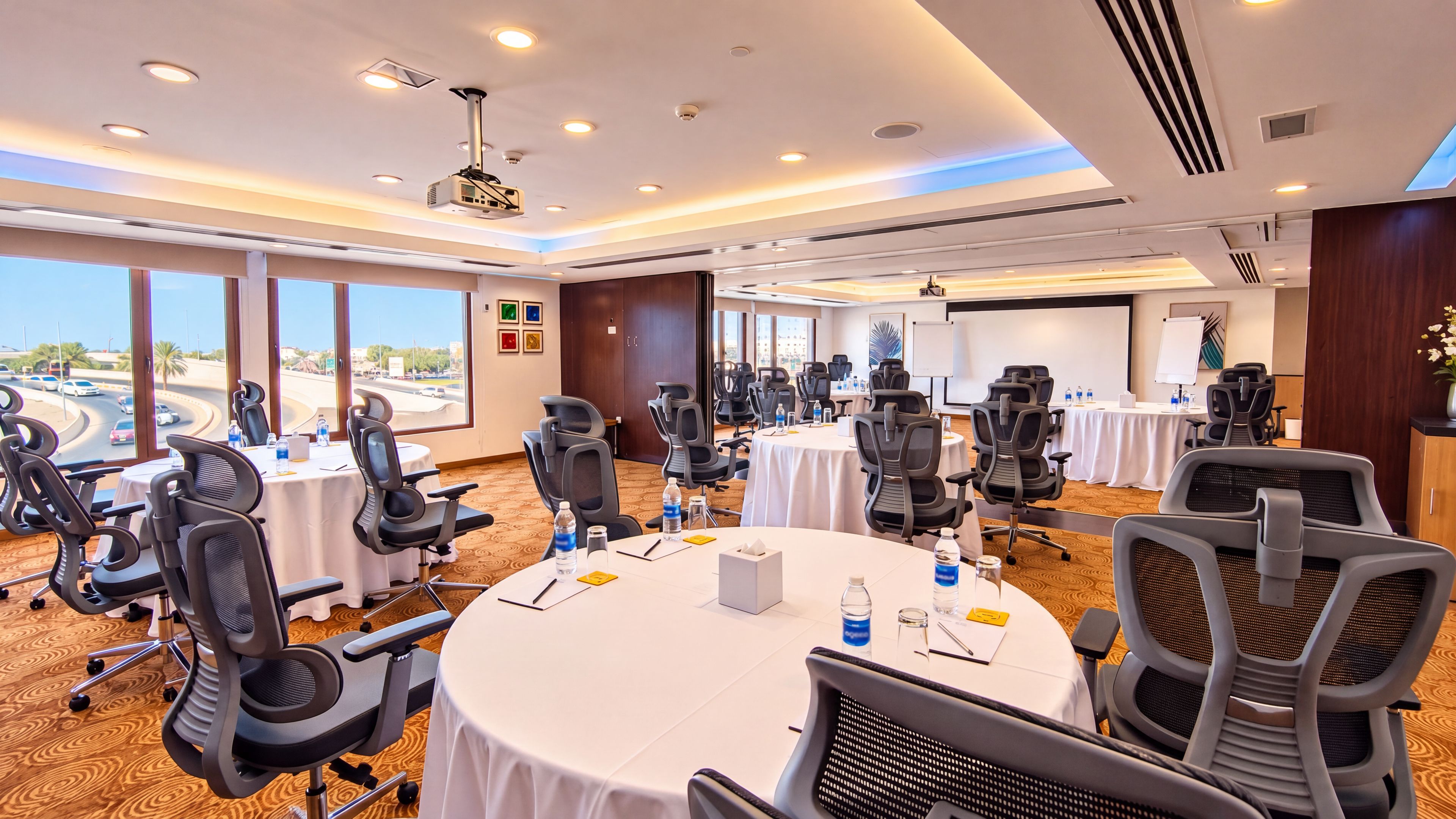 A conference room with multiple tables and chairs, large windows, and a projector.