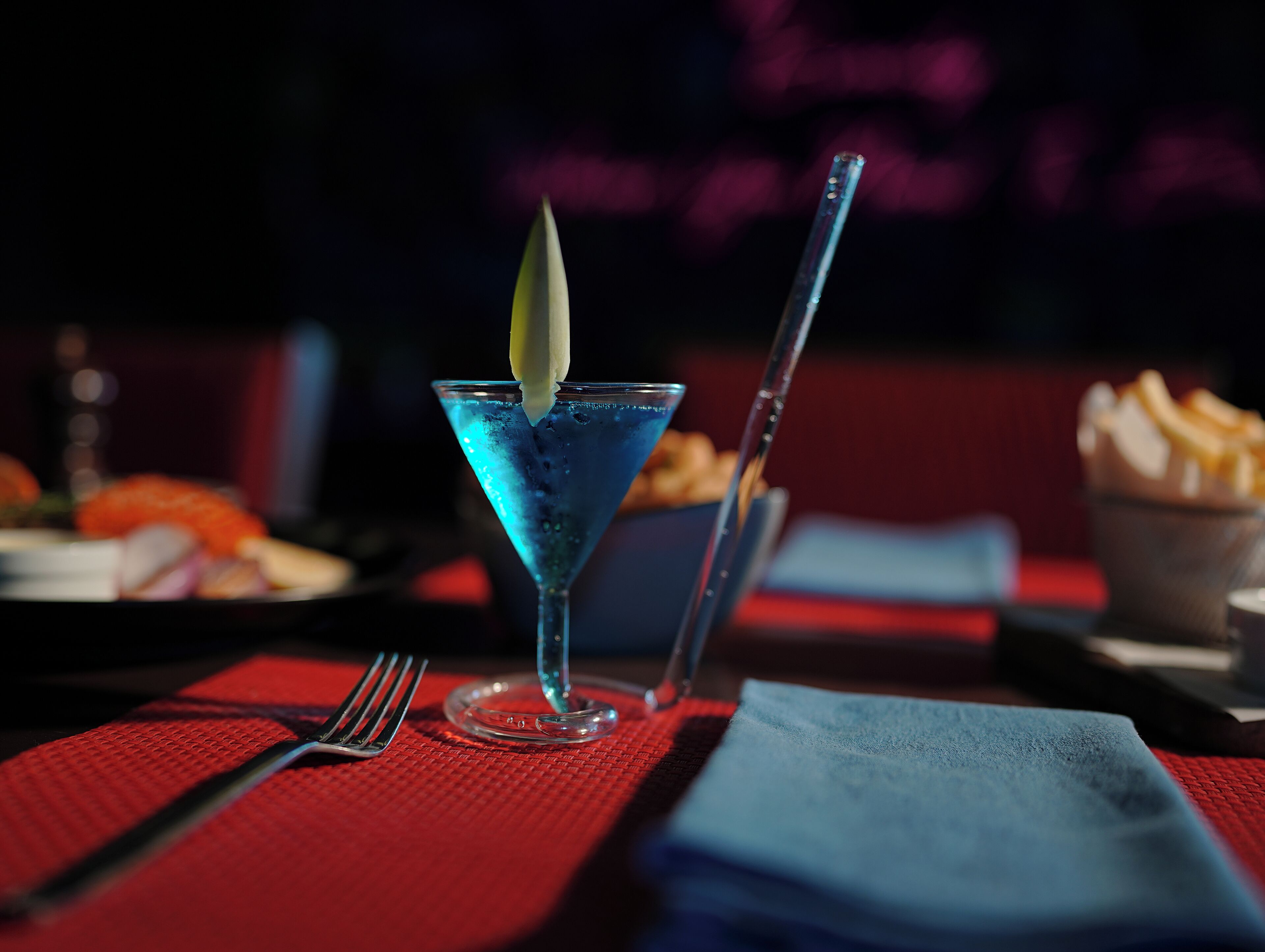 Een martini glas met een blauwe drank en een limoenpartje op een rode tafelkleed.