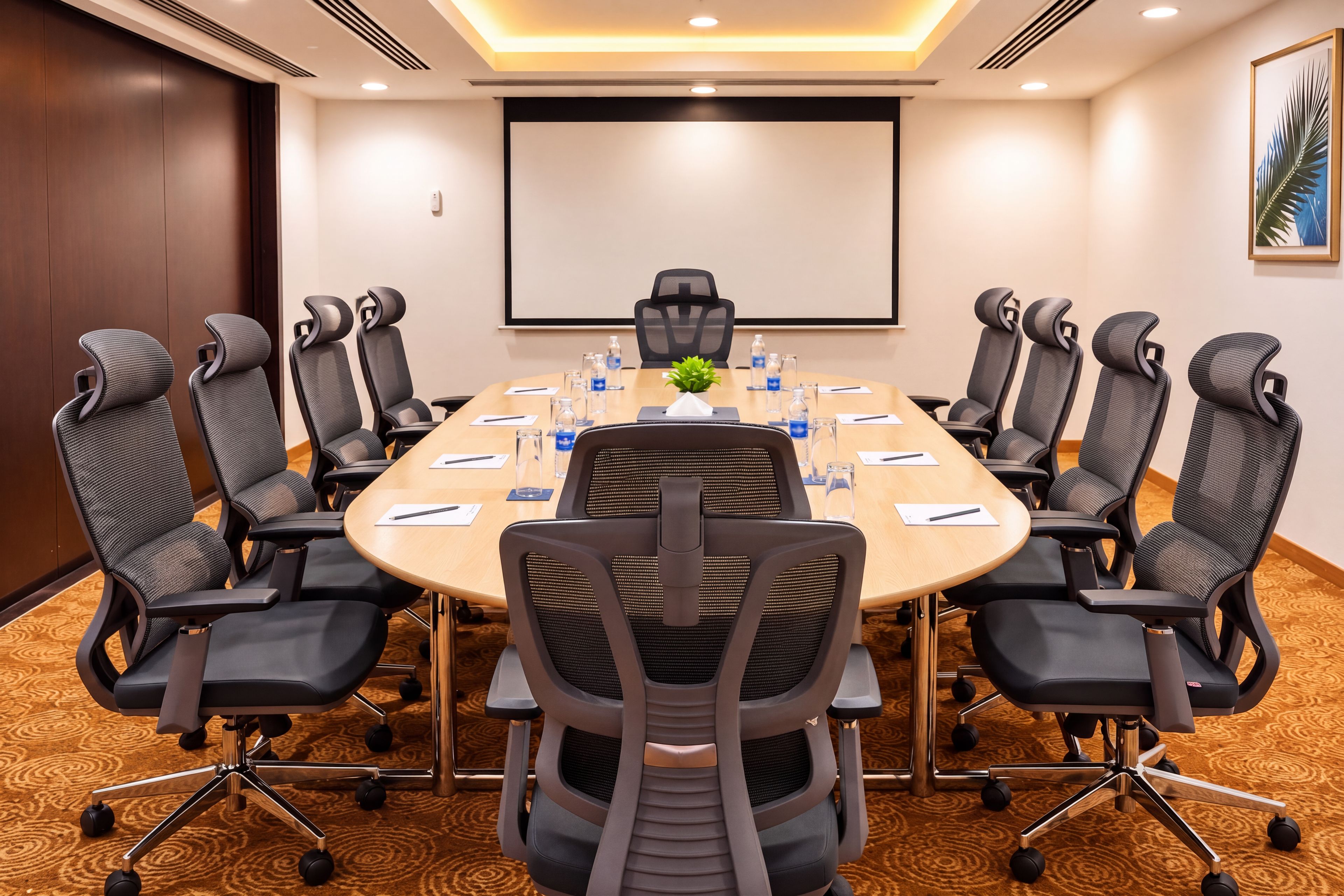A conference room with a round table, eight chairs, and a projector screen.