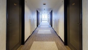 Un largo y estrecho pasillo de hotel con puertas a ambos lados, suelo alfombrado e iluminación en el techo.