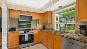 Une cuisine moderne avec des meubles en bois, des appareils électroménagers en acier inoxydable, un plan de travail en granit et une vue sur un quartier résidentiel.