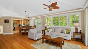 Un salon spacieux doté d’un ventilateur de plafond, un coin repas avec des chaises en bois, un canapé et une table basse.