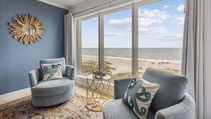 A room with two grey armchairs, a round mirror, and a view of the beach.