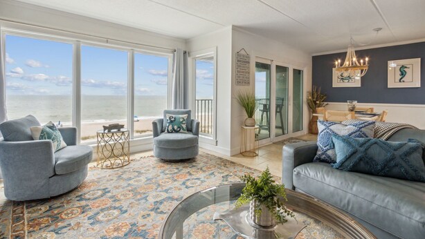 A spacious living room with a large window overlooking the ocean, a ceiling fan, and a chandelier.