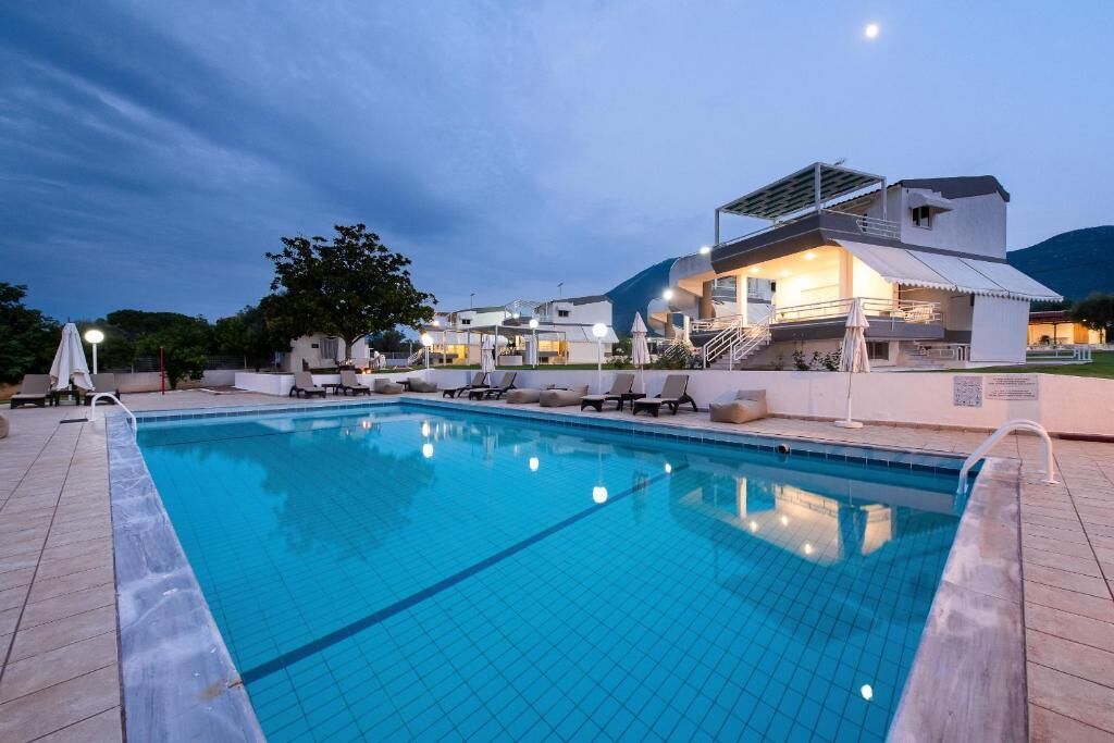 A swimming pool with lounge chairs and a building with a covered deck in the background.