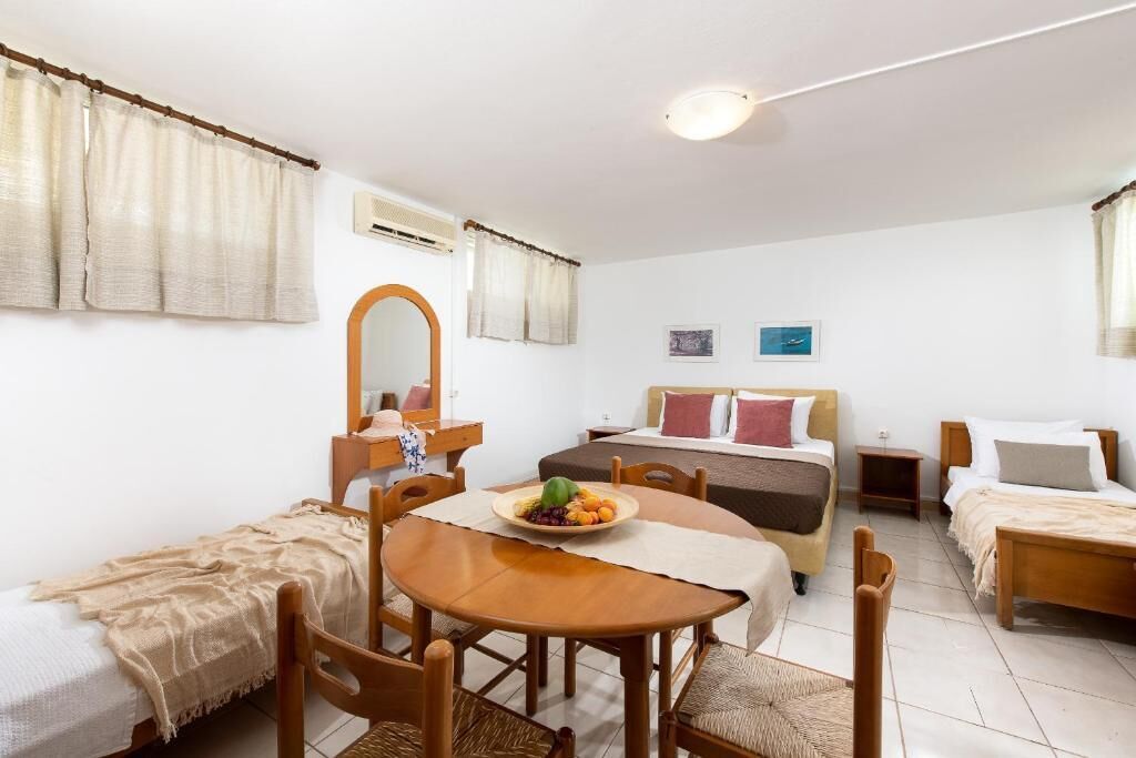 A room with a bed, a desk, a chair, a table with a fruit bowl, and a mirror.