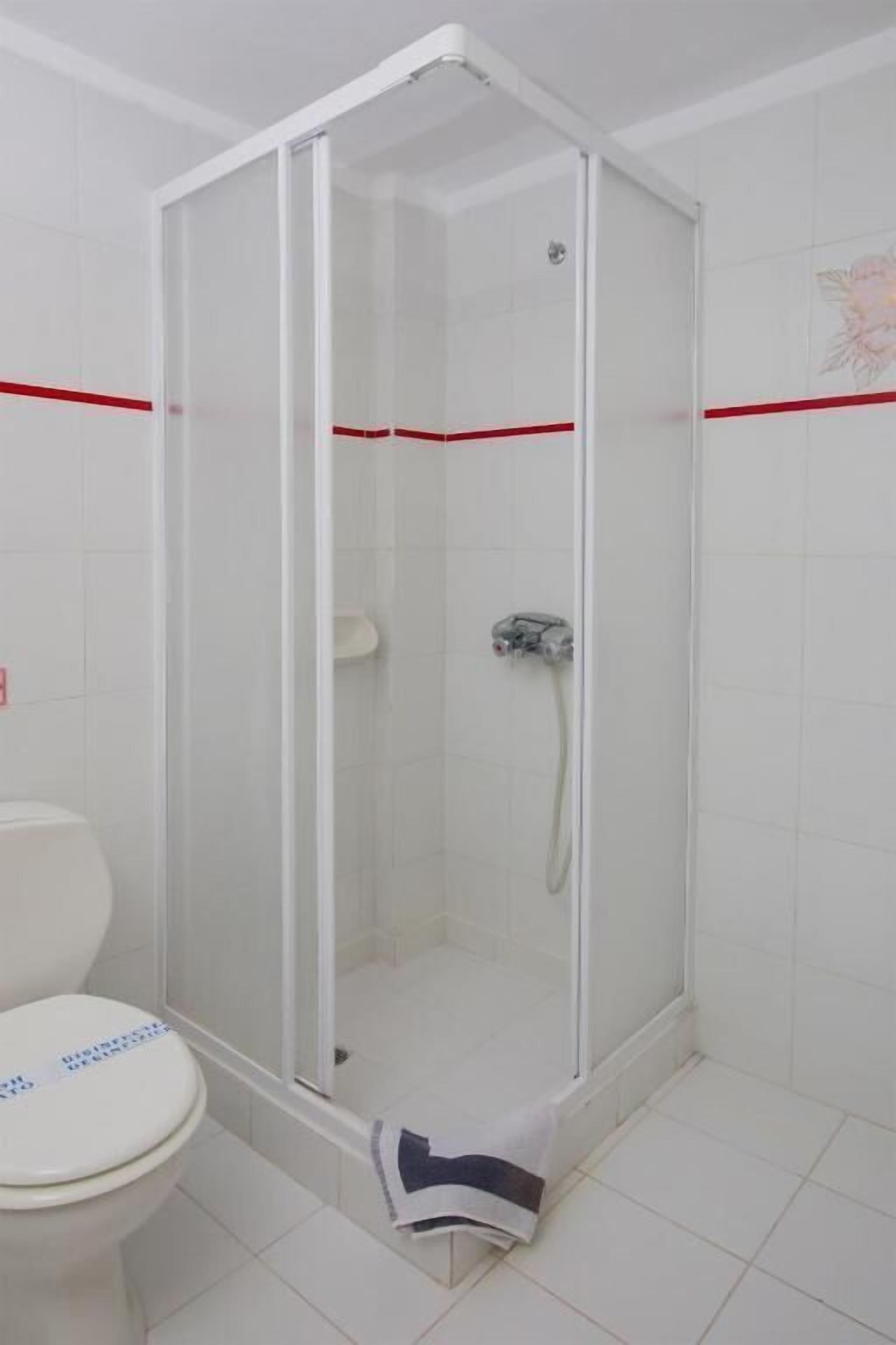 Een badkamer met een douchecabine van glas, een toilet en witte betegelde wanden.