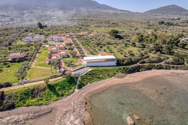 An aerial view of a coastal property with multiple buildings, a large white structure, and a beach area. - Blue Marine Village (Chalcis)