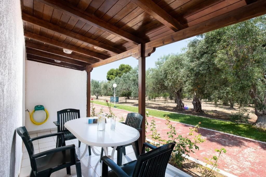 A covered patio with a round table and chairs, overlooking a garden with trees and a pathway.