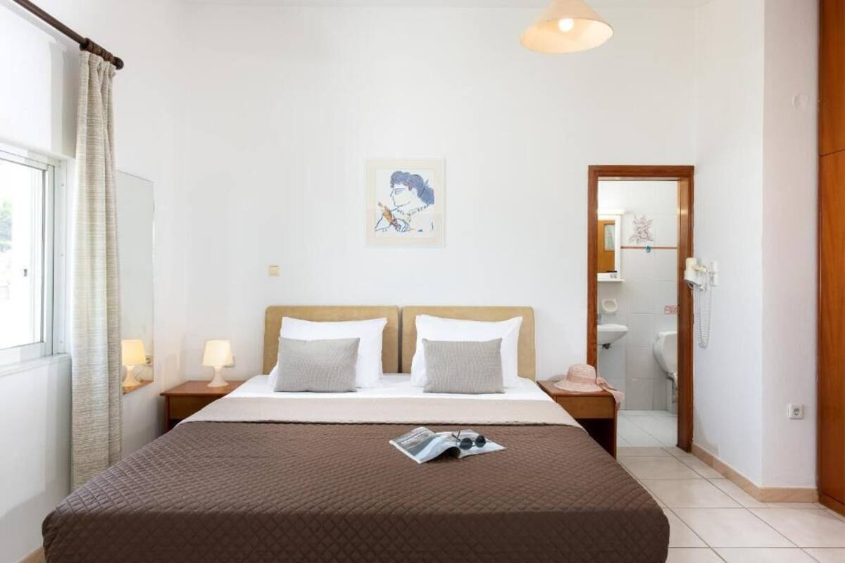 A hotel room with a large bed, two bedside tables with lamps, a framed artwork on the wall, and a bathroom visible through an open door.