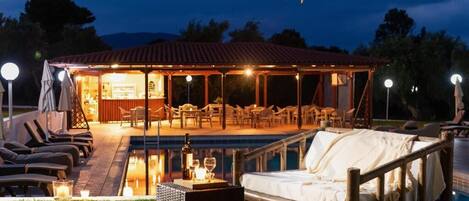 A poolside lounge area with a covered seating area, a pool, and a dining setup.