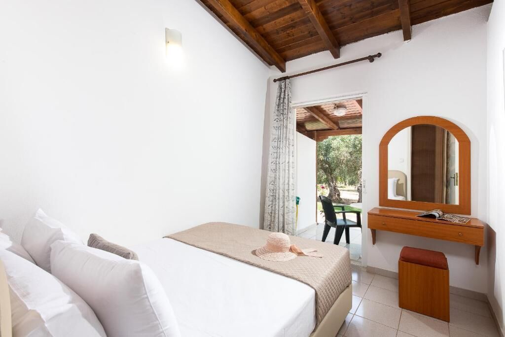 Un dormitorio con cama, un escritorio de madera, un espejo y vistas al exterior.