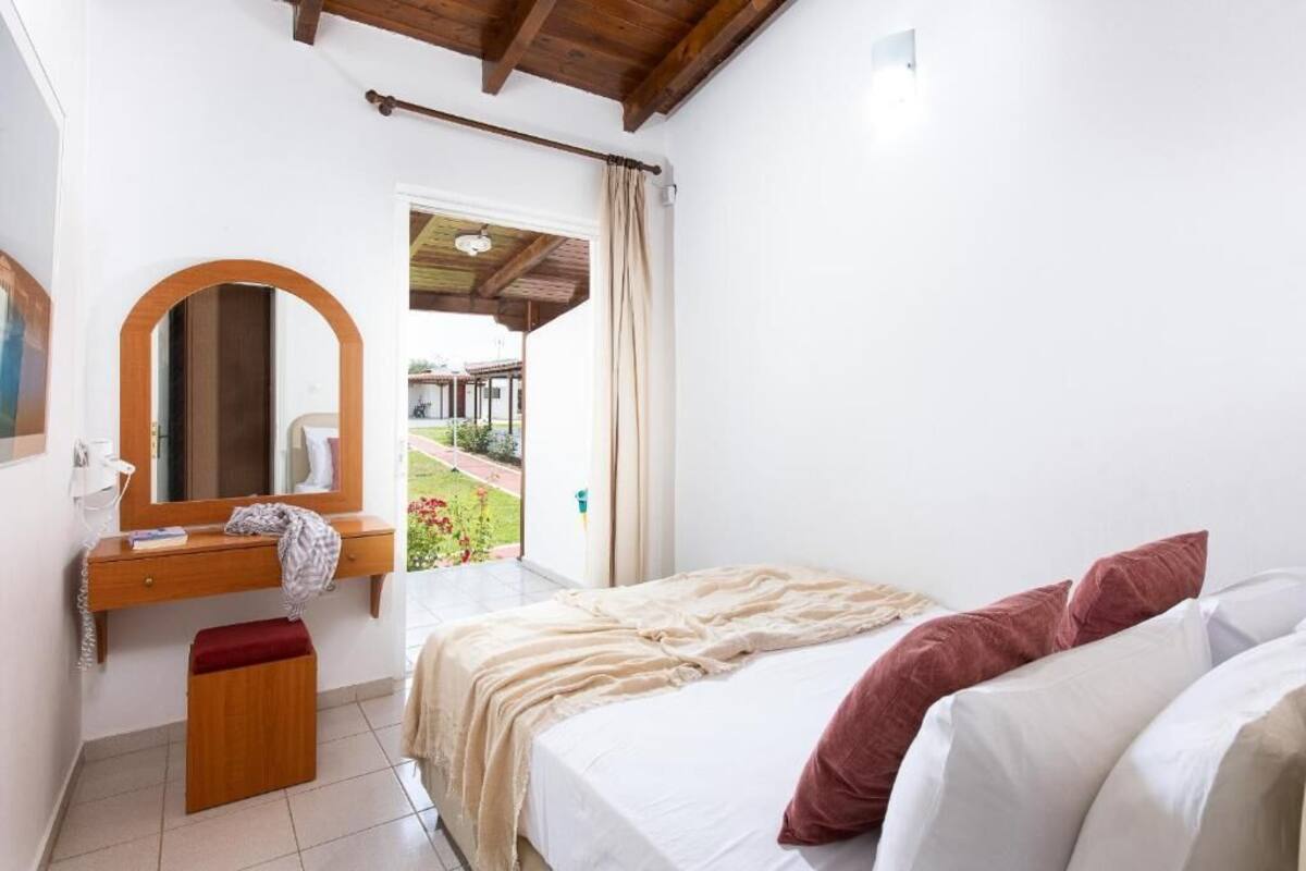 A bedroom with a bed, a wooden dresser, a mirror, and a view of a garden through an open door.