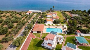 An aerial view of a coastal property with a swimming pool, multiple buildings, and a view of the sea. - Blue Marine Village (Chalcis)