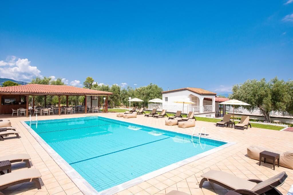 A swimming pool with lounge chairs and umbrellas, surrounded by buildings and trees.