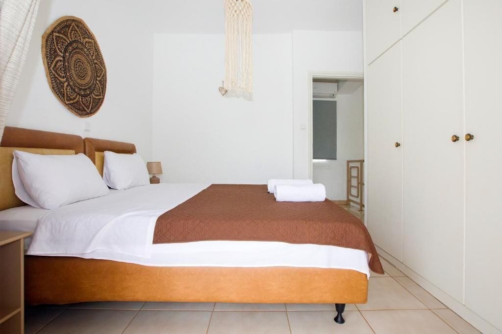 A bedroom with a bed, white walls, a wooden headboard, a decorative wall hanging, and a door with a handle.