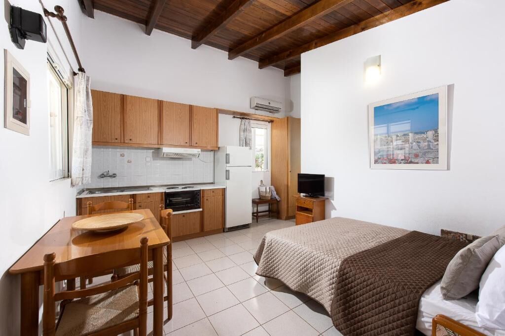 Habitació senzilla amb llit, taula de fusta, televisió i petita cuina.