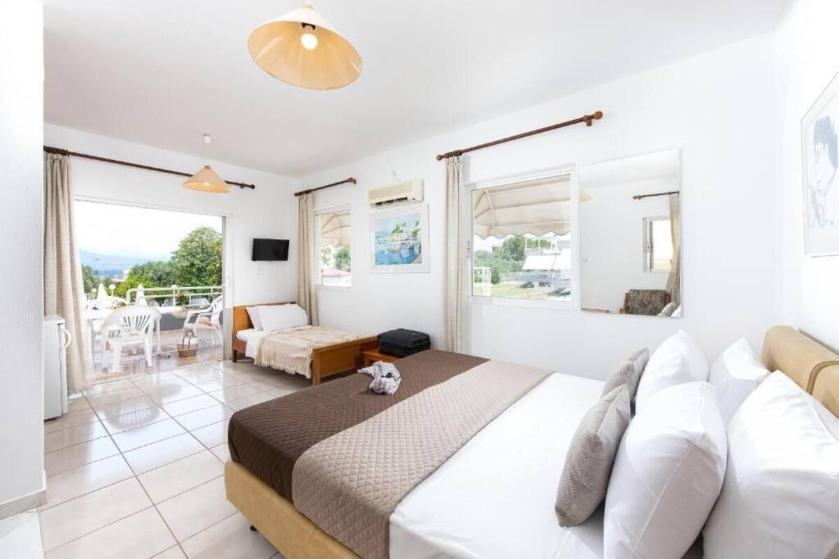 A hotel room with a bed, a desk, a chair, and a balcony with outdoor furniture.