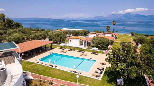 A resort with a swimming pool, lounge area, and a view of the sea and mountains. - Blue Marine Village (Chalcis)