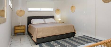 Un dormitorio con cama, mesita de noche, lámpara y una silla.