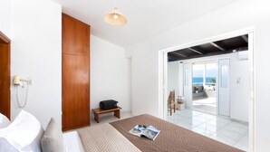 A bedroom with a bed, a wooden wardrobe, a bench, and a view of the sea through an open door. - Blue Marine Village (Chalcis)