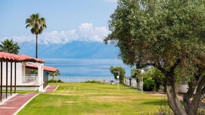 A coastal property with a grassy lawn, a red-roofed building, and a view of the sea and mountains. - Blue Marine Village (Chalcis)
