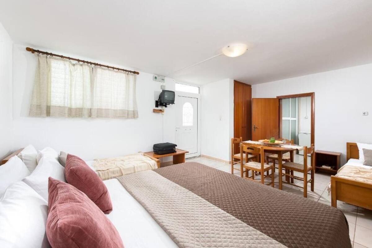 A room with a bed, a desk, and a chair. There is a television on the wall and a window with curtains.