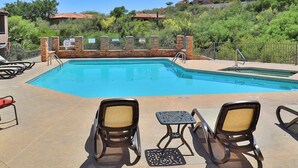 A swimming pool with lounge chairs and a table, surrounded by a brick wall and a metal fence. - Catalina Foothills Condo on the Golf Course (Tucson)