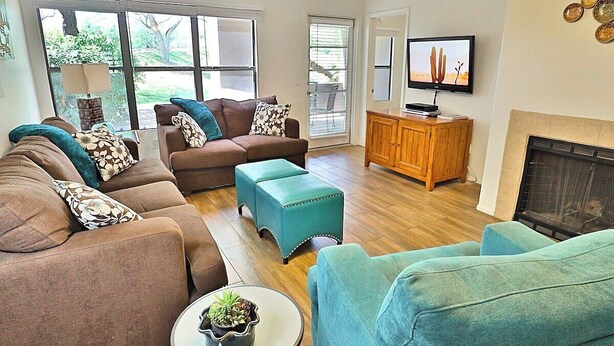 A living room with a sofa set, ottomans, a television, and a fireplace. - Catalina Foothills Condo on the Golf Course (Tucson)