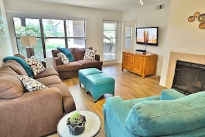A living room with a sofa set, ottomans, a television, and a fireplace.